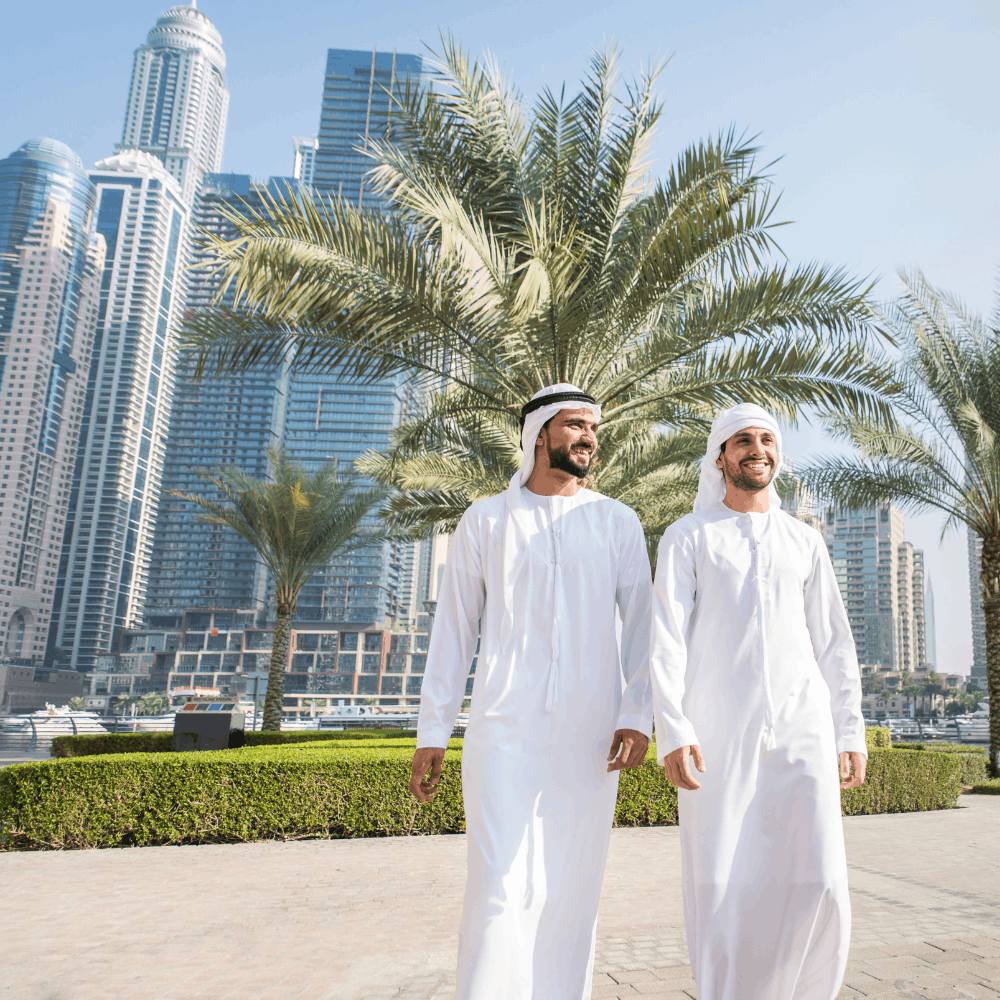 two men walking in Dubai with palm trees and buildings behind them